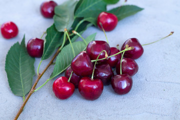 fresh red cherries with green leaves on a grey background