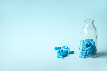 Blue homeopathic capsules and glass bottle on blue background with copy space for text. Spilled capsules on a blue background next to a glass bottle.