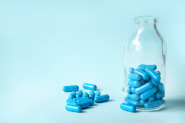 Blue homeopathic capsules and glass bottle on blue background with copy space for text. Spilled capsules on a blue background next to a glass bottle.