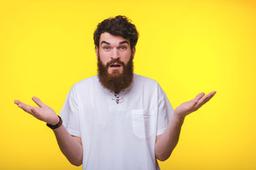 Bearded man is showing that he is astonished with bosth hands up near yellow wall.
