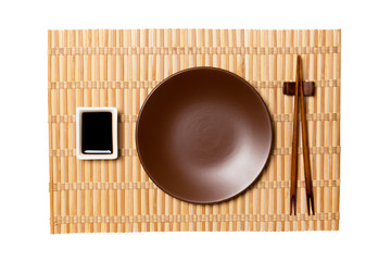 Empty round brown plate with chopsticks for sushi and soy sauce on yellow bamboo mat background. Top view with copy space for you design