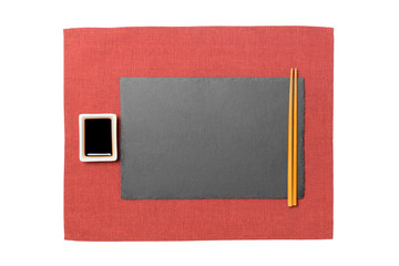 Empty rectangular black slate plate with chopsticks for sushi and soy sauce on red napkin background. Top view with copy space for you design