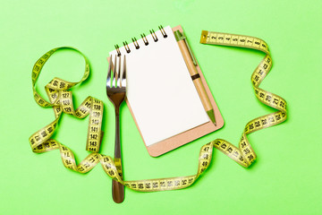 Fitness concept with empty space for your design on green background. Top view of notepad and fork surrounded with yellow measure tape