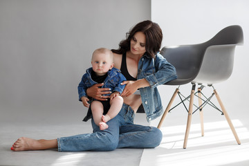 Young woman mother in denim overalls holds a baby child in her arms. White background in the...