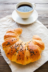 croissant and a cup of instant coffee on a textured wooden background top view, cozy and delicious Breakfast. Rustic background