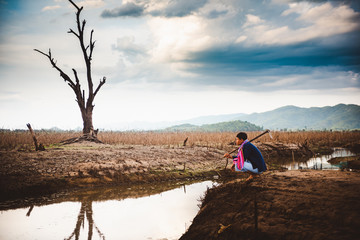 Water crisis concept, Hopeless and lonely farmer sit on cracked earth near drying water.