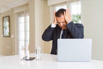 Middle age business man working with computer laptop suffering from headache desperate and stressed because pain and migraine. Hands on head.