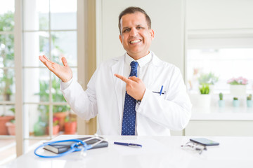 Naklejka na ściany i meble Middle age doctor man wearing medical coat at the clinic amazed and smiling to the camera while presenting with hand and pointing with finger.