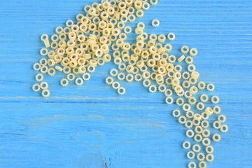 Tiny round italian pasta with selective focus on blue textured wooden background. Uncooked noodles on wood backdrop. Raw organic vegetarian noodle. Small round rings pasta for soup. Food background 