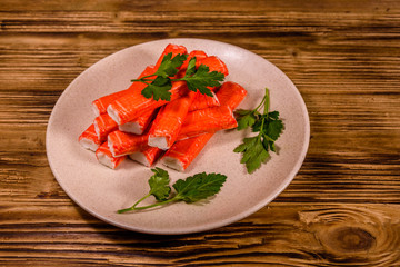 Ceramic plate with pile of crab sticks and parsley twig on a wooden table