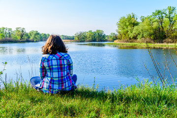 Fototapeta premium Lonely young woman sitting on a bank of the river