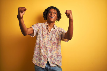 Afro man with dreadlocks on vacation wearing floral shirt over isolated yellow background very...