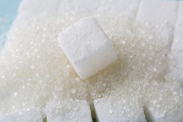 Heap of granulated sugar with cube on blue background. 