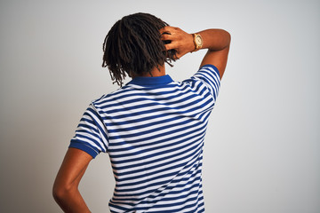 Afro man with dreadlocks wearing striped blue polo standing over isolated white background Backwards thinking about doubt with hand on head