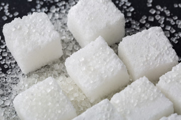 Closeup of granulated and sugar cube on black background
