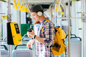 Young aman is standing in a bus with headset on his head and listening to the music.
