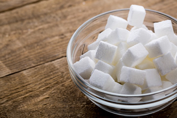 Closeup of sugar cubes in glass bowl on wooden table.