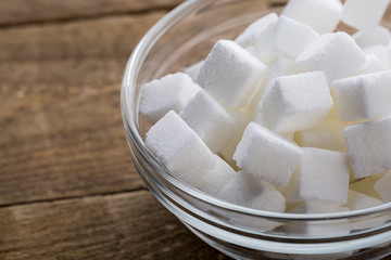 Closeup of sugar cubes in glass bowl on wooden table.