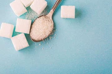 Top view of granulated sugar in spoon with cube on blue background.