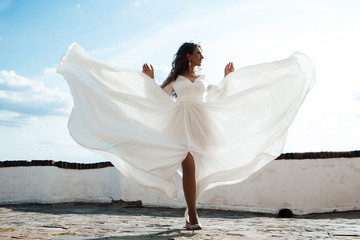 Fototapeta na wymiar Fashion girl in beautiful luxury white flowing silk dress, Woman in long flying evening dress with a gown, Stunning fantasy model. Silk fabric waving on wind. Satin Cloth Flowing, Waves of a dress