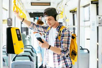 Young man is standing in a bus with headset on his head and listening to the music.
