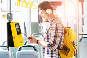 Young aman is standing in a bus with headset on his head and listening to the music.