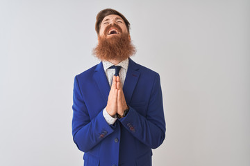Young redhead irish businessman wearing suit standing over isolated white background begging and...