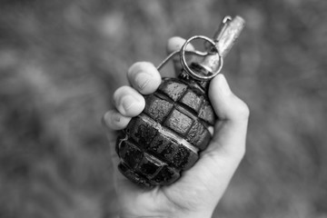 Closeup top view of white kid hand holding real old grenade. Horizontal black and white photography.