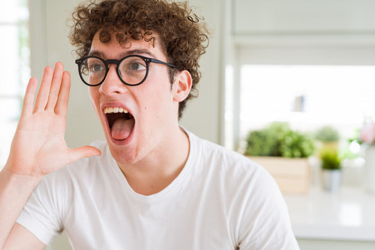 Young handsome man wearing glasses shouting and screaming loud to side with hand on mouth. Communication concept.