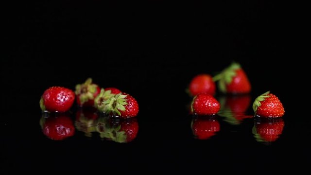 Fresh ripe strawberries falling on wet black surface