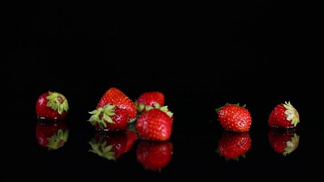 Fresh ripe strawberries falling on wet black surface
