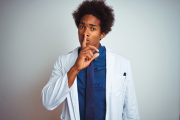 Fototapeta na wymiar Young african american doctor man wearing coat standing over isolated white background asking to be quiet with finger on lips. Silence and secret concept.