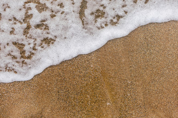 Fototapeta na wymiar Beautiful natural border or frame formed by white foamy sea water splashing at sandy beach outside. Horizontal color flatlay photography.