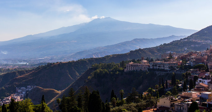 Beautiful panorama on the smoking Etna Mount from Taormina, a sunny summer day in Sicily (Italy). Blue sky, green vegetation and pink houses in the foreground. – Image