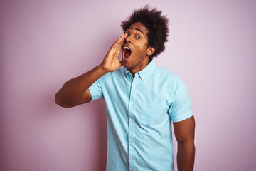 Young american man with afro hair wearing blue shirt standing over isolated pink background shouting and screaming loud to side with hand on mouth. Communication concept.