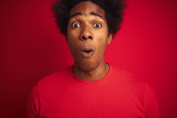 Fototapeta na wymiar Young american man with afro hair wearing t-shirt standing over isolated red background scared in shock with a surprise face, afraid and excited with fear expression