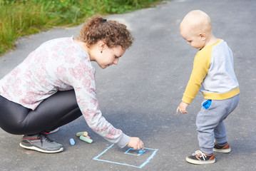Fototapeta premium Mother with her little son draws a colorful chalk on asphalt on a summer day. Mom and child activity.