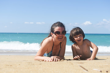 Fototapeta premium Mom with the small son On beach in the sea waves. Happy family enjoy at beach. Summer vacation, smiling and joy in waves