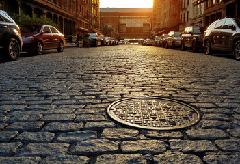 Sunlight shining on a cobblestone street and manhole cover in New York City