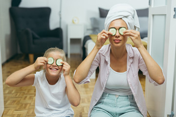 mother and daughter putting cucumber on theirs face at home