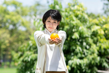 Happy asian woman holding orange in garden. Smiling people with blurry background.