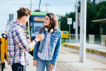 Fototapeta premium Outdoor shot of attractive millennial couple dressed casual drinks coffee from disposable cup, wanders around city, enjoys leisure time.