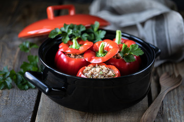 Red pepper stuffed with meat in a black pan on a wooden table.