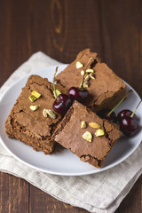 Homemade Dark Chocolate Brownies Cake Topping with Pistachios and Cherry on White Plate on Wooden Table Vertical Delicious Bitter Sweet and Fudge Chocolate Cake Dessert