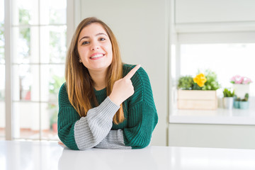 Naklejka premium Young beautiful plus size woman wearing casual striped sweater cheerful with a smile on face pointing with hand and finger up to the side with happy and natural expression
