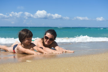 Mom with the small son On beach in the sea waves. Happy family enjoy at beach. Summer vacation, smiling and joy in waves