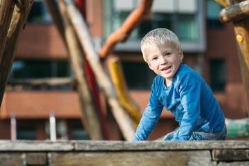 Cute happy baby boy with blond hair having fun on the playground on sunny summer day .
