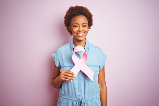 Young african american woman holding brest cancer ribbon over isolated pink background with a happy face standing and smiling with a confident smile showing teeth