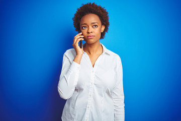 African american woman talking on the smartphone over blue isolated background with a confident expression on smart face thinking serious