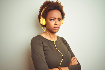 African american woman wearing headphones listening to music over isolated background skeptic and...